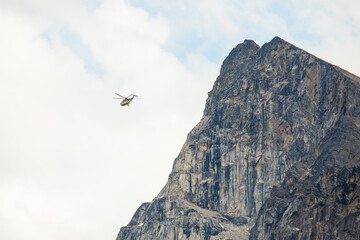 Helicopter flies next to mountain cliff.