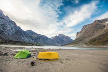 Tents set up on a sandy beach below mountain peaks.