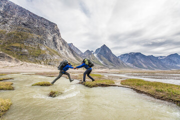 Backpackers work together to cross a river channel.