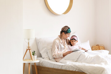 Little girl with her mother reading fairy-tale in bedroom