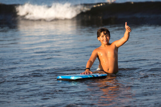 Nine year-old boy giving thumbs-up sign in water after boogie boarding
