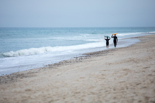 mother and son in distance walking down beach carrying boogie boards