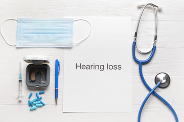 Text HEARING LOSS with stethoscope, medical mask and aid on white wooden background