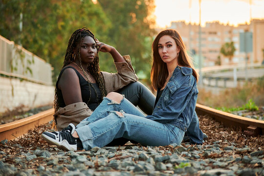 Two multi-ethnic young women pose and look at the camera at sunset