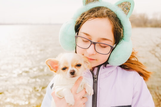 Portrait of a happy teenage girl with her small chihuahua dog. A girl on the background of nature hugs her Chihuahua dog in clothes.