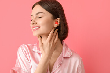Young woman with ear plug on pink background