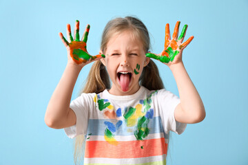 Little girl with hands in paint showing tongue on blue background
