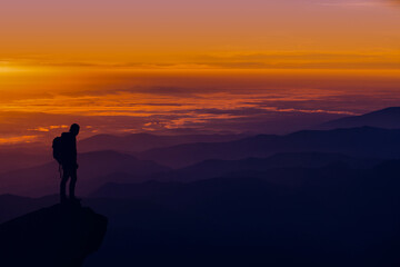 Fototapeta na wymiar A man standing on top of a mountain as the sun sets. Goals and achievements concept photo composite.