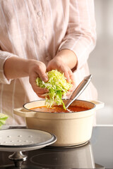 Woman adding cabbage to cooking pot with borscht in kitchen