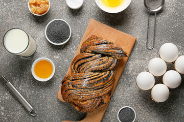 Wooden board with tasty poppy seed bun and ingredients on grunge background