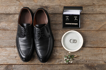 Fototapeta na wymiar Tray with wedding rings, groom shoes and stylish male accessories on wooden background