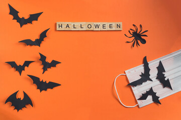 Halloween inscription made from wooden cubes and bats cut from black paper on an orange background with a protective medical mask. Holidays during quarantine. Paper cut style.Flatlay, Copy Space