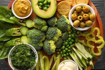 Stand with different green vegetables and bowls with sauce on dark wooden background, closeup