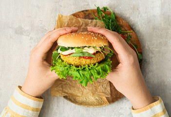 Woman holding tasty vegetarian burger on grunge background