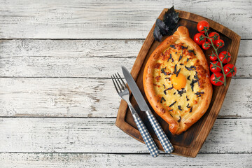 Board with tasty Ajarian khachapuri on light wooden background