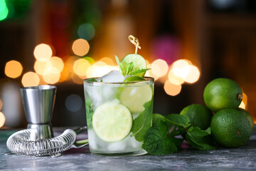 Glass of cold mojito on table against blurred lights