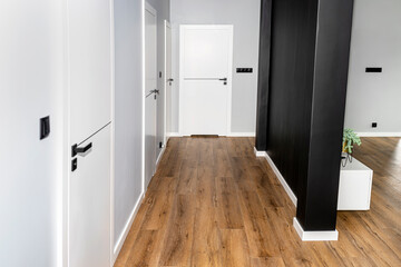 A white door with a ventilation undercut with a matte black handle and a black line in the middle in a modern house with vinyl panels on the floor.