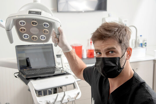 Retrato de un odontólogo con barbijo en su consultorio, manipulando las luces de exploración