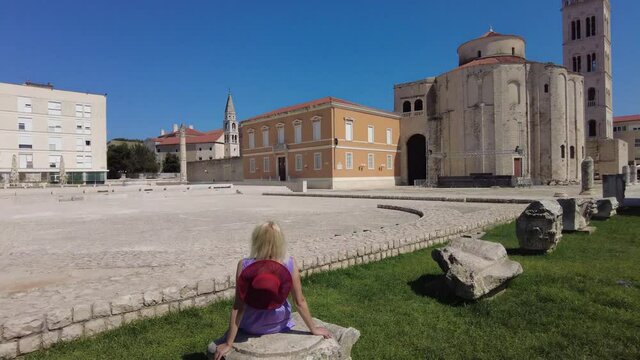 Woman with hat in the Ancient Roman Forum of Zadar city of Croatia on Adriatic Sea and capital of Dalmatia. Roman square with Church of St Donatus and Cathedral of St. Anastasia with the bell tower.