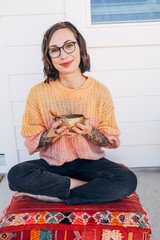 Portrait of smiling woman sitting in yoga pose holding brass singing bowl