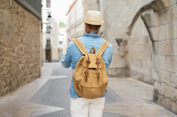 Rear view of a young man with backpack walking on the street in the old town. High quality photo.