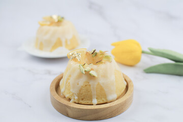Homemade lemon cake classic recipe, decorated with sugar icing on marble table. Healthy organic summer dessert pie with yellow tulip on background. 