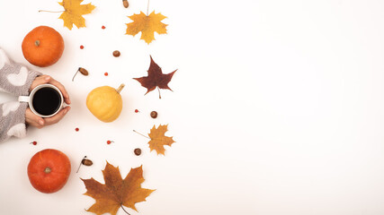 A woman holds a cup of black coffee near the yellow maple leaves of a pumpkin on a white background. Autumn flat lay.
