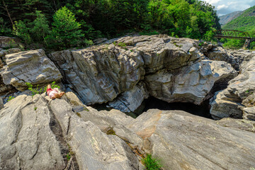 Woman among gorges of canyon of Aussichtspunkt Ponte Brolla bridge in Ticino Switzerland. Ponte Brolla is a famous attraction where you can sunbathing, canyoning and climbing. River Maggia by Locarno