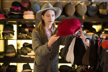 Young focused woman shopping hats in modern store