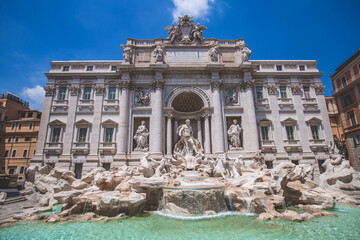 Daytime front view photo of the Trevi Fountain (Fontana di Trevi) in Rome, Italy with a blue sky.