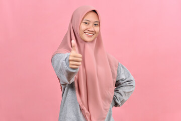Fototapeta premium Young Asian Muslim woman showing thumb up against pink colour background.