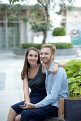 Hugging beautiful young boyfriend and girlfriend sitting on bench in park and looking at camera