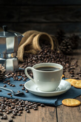 Hot coffee in a white coffee cup and many coffee beans placed around and sugar on a wooden table in a warm, light atmosphere, on dark background.