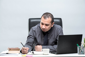 Asian male office worker sitting in front of a laptop computer at a desk and smiling at the office