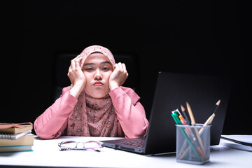 A picture of an office worker, a Muslim woman, who is working overtime at the office with a weary face and tired from working all day.