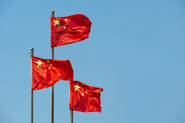 Three red Chinese flags waving in the wind on a blue sky background