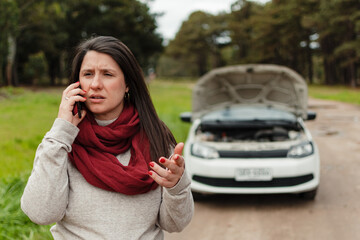 close-up of latina woman talking on cell phone and gesticulating. Her broken car in the background