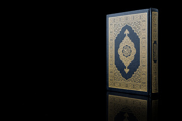 Islamic concept - The Holy Al Quran with written Arabic calligraphy meaning of Al Quran, Arabic word translation: The Holy Al Quran (holy book of Muslim), on black background, with copy space.