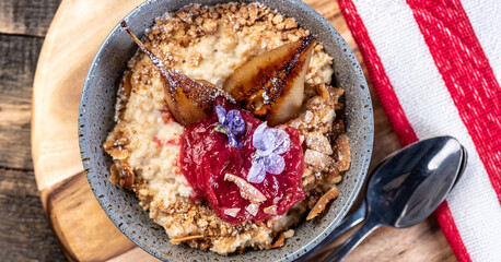 A bowl of warm oatmeal served with pear pieces on a wooden serving board with a red and white towel