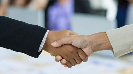 Selective focus on business women's hands in formal suits doing hand shake during business meeting with blurry colleagues in background. Concept for business meeting