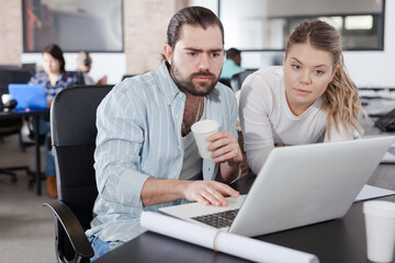 Positive young business woman explaining new project to male coworker, pointing at laptop screen