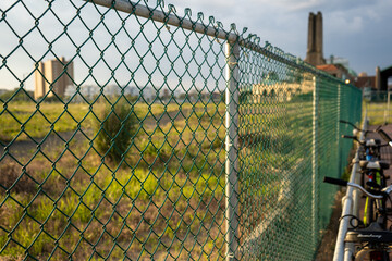 Closeup of chain link fence, long perspective view past bikes and field towards buildings in the distance.