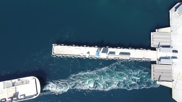 Ferry using energy to push water against pier in Lavik Norway during departure and moves out of frame - Ferry Oppedal along road E39 - Norway birdseye aerial - Symbol of spending energy to move ship
