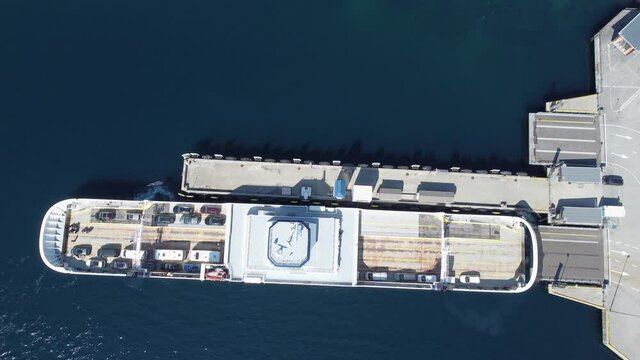 Car ferry Mf Oppedal leaving port of Lavik on road E39 after beeing fully loaded - Static birdseye aerial at departure - Norway