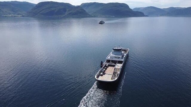 Ferry Oppedal from Norled company is transporting cars and passengers across Norwegian Sognefjord during sunny summer day - Aerial above and behind ferry during open sea crossing
