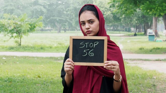 Afghan girl holding Blackboard with Stop 5G written. Portrait of serious Afghan eco-activist protesting against harmful impact of mobile towers.Concept of technological pollution,telecommunication, 5G