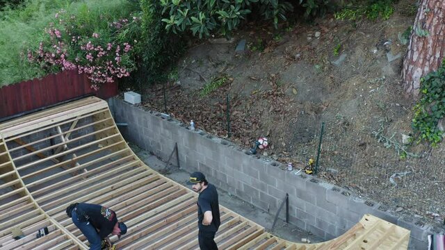 Two Young Men Making A Skate Ramp In Backyard. Tilt Down Reveal Shot.