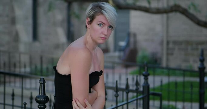 Sad lonely and depressed short haired blonde lady leaning against rail at cemetery church after the passing of a loved one from Covid in 2021. In Cinema 4K (4096x2160) 30fps slowed from 60fps.