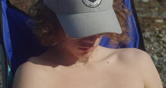 Young Shirtless Man In Cap Relaxing Under The Sunlight At Coverack Beach At The Lizard Peninsula In Cornwall, UK. close up