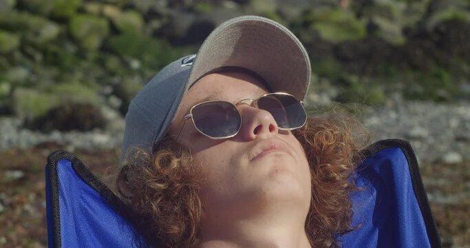 Close Up Of Male Tourist In Cap And Sunglasses Relaxing Under The Sunlight At The Beach.